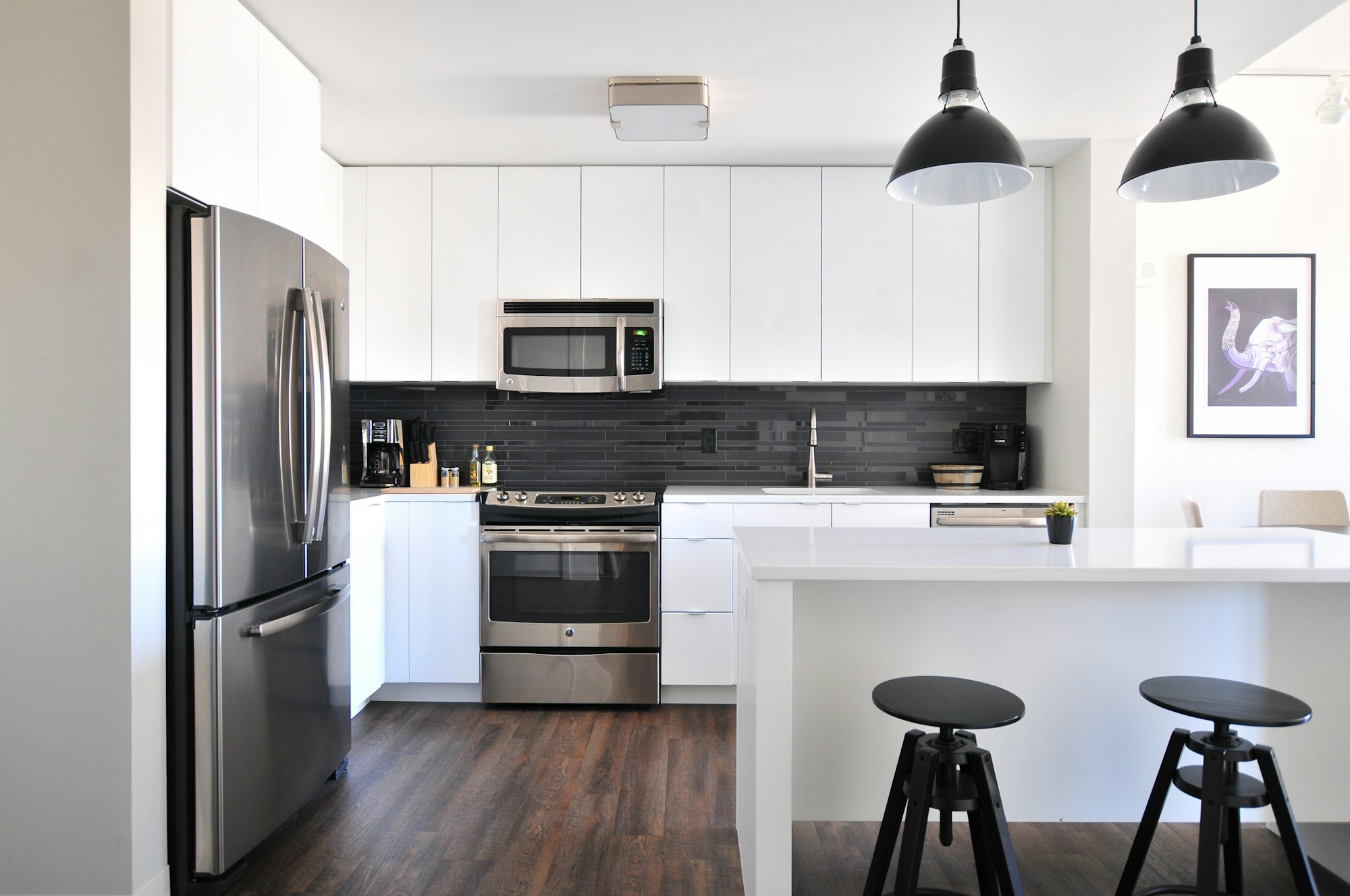 Renovated open-plan kitchen with dark cabinetry, marble island, and warm pendant lighting