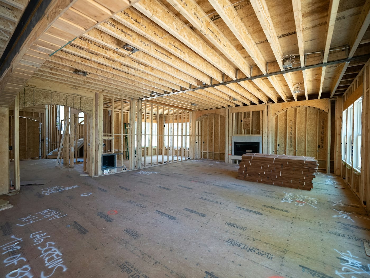 Open main floor framed out on a job site, engineered joists overhead and flooring stacked ready to lay